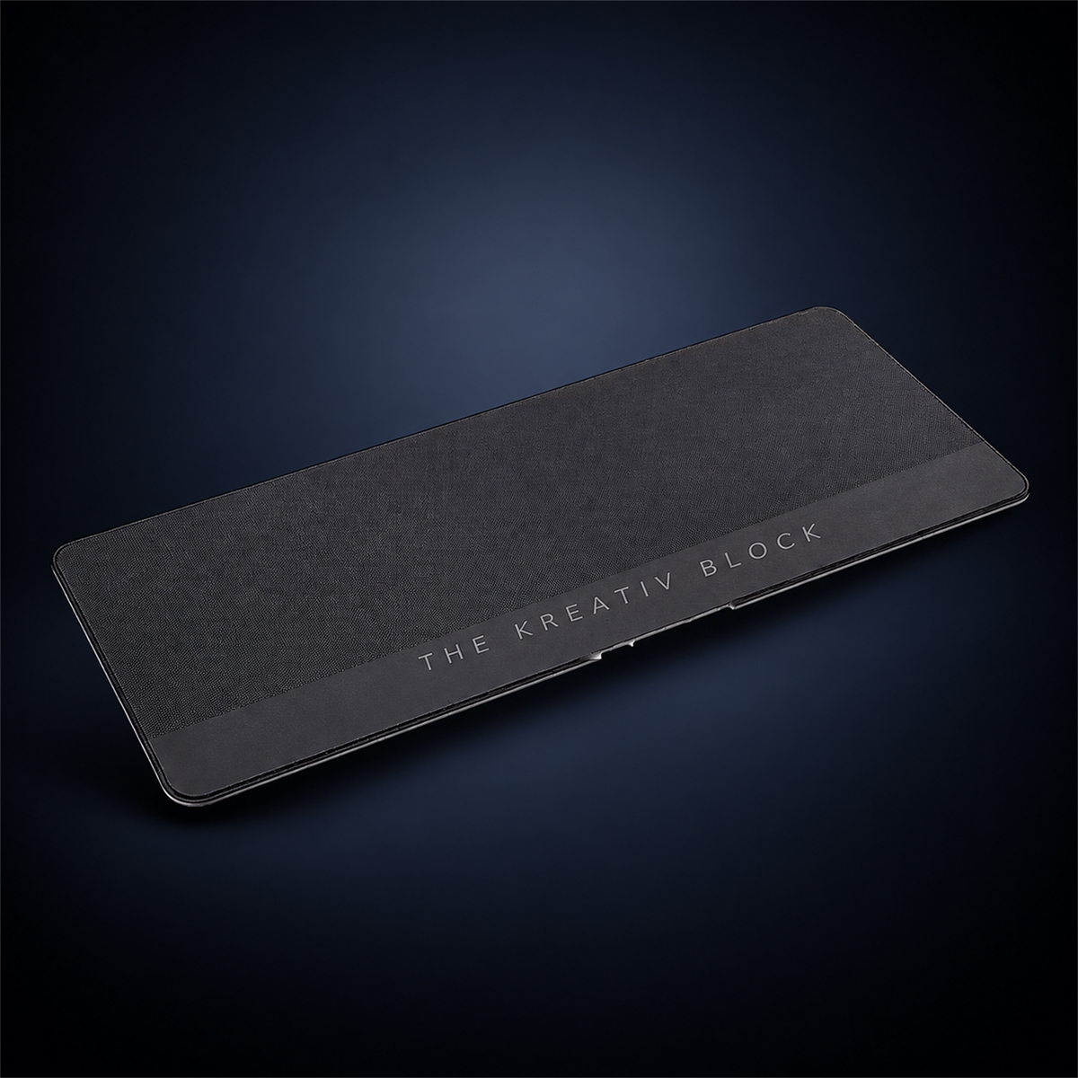 Studio concept image of a wide dark textured founder desk mat with The Kreativ Block branding along its lower edge.